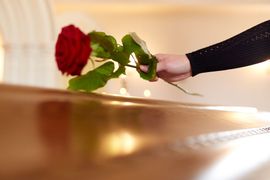 hand laying rose on coffin