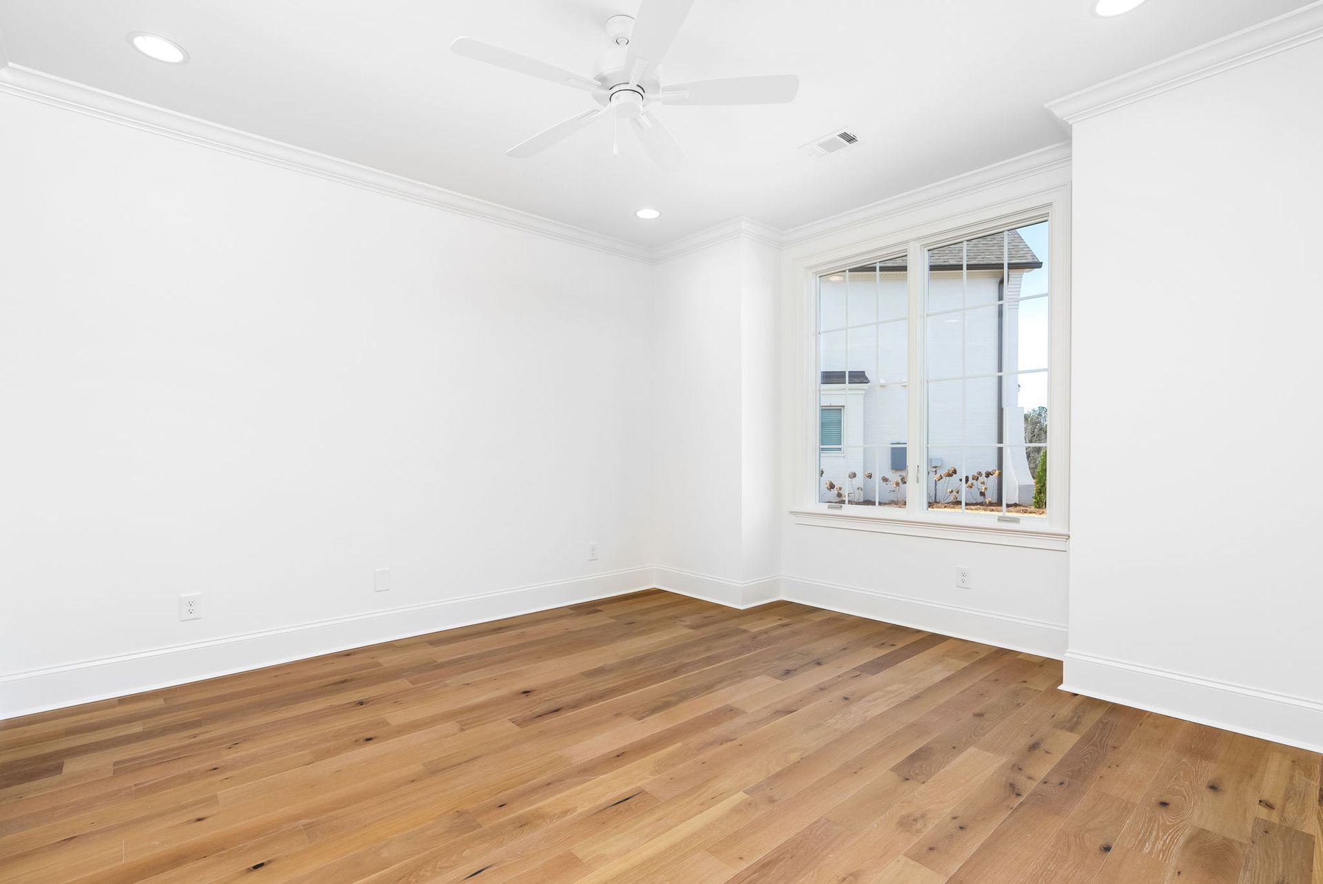 An empty room with hardwood floors and a ceiling fan.