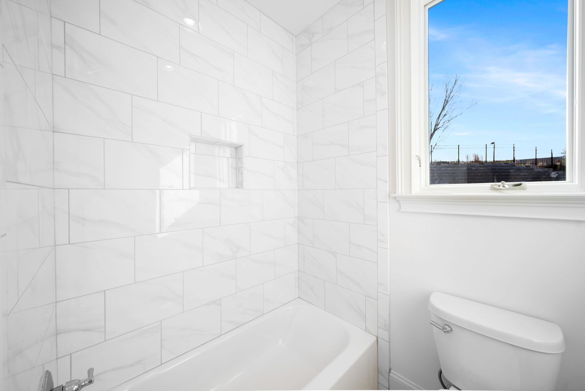 A bathroom with a tub , toilet , and window.