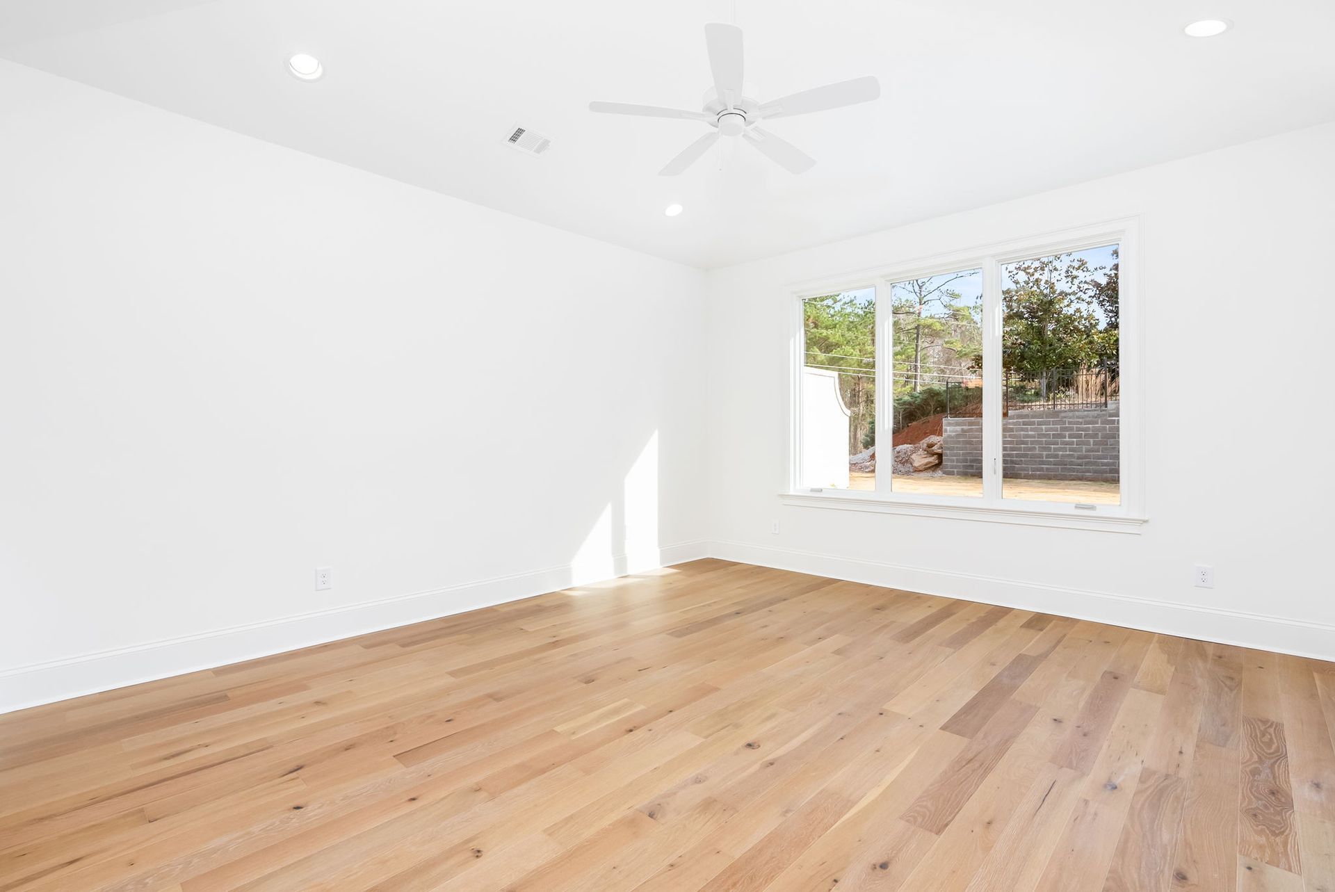 An empty room with hardwood floors and a ceiling fan.