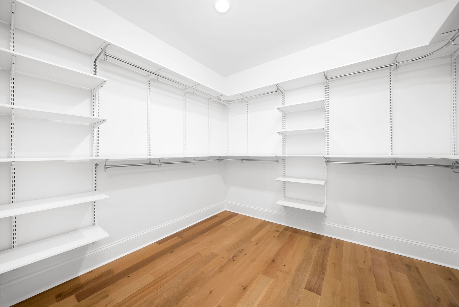 An empty walk in closet with wooden floors and white shelves.
