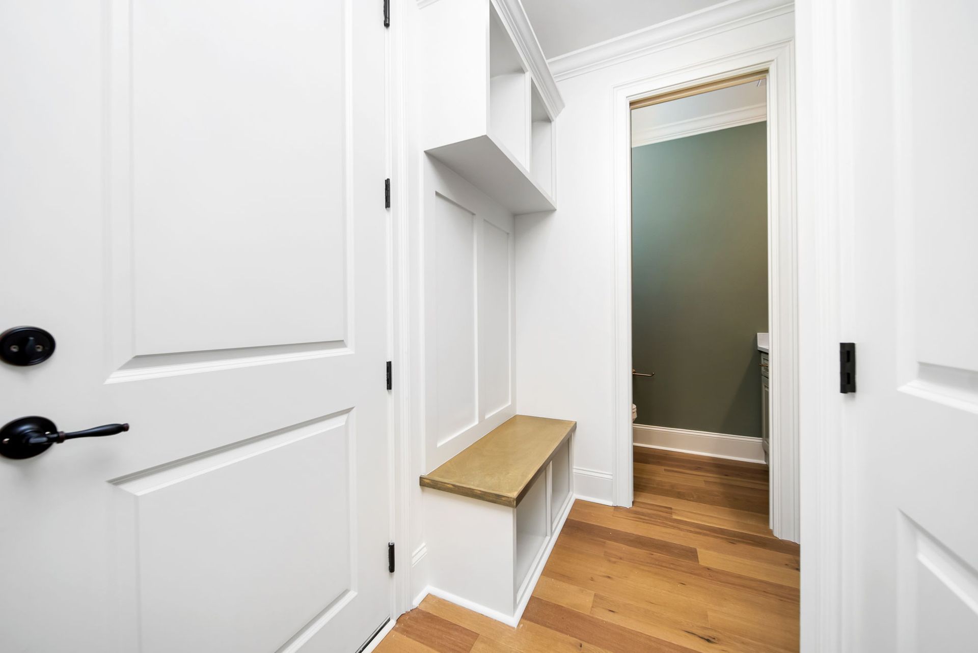 A hallway with white doors and wooden floors leading to a bathroom.