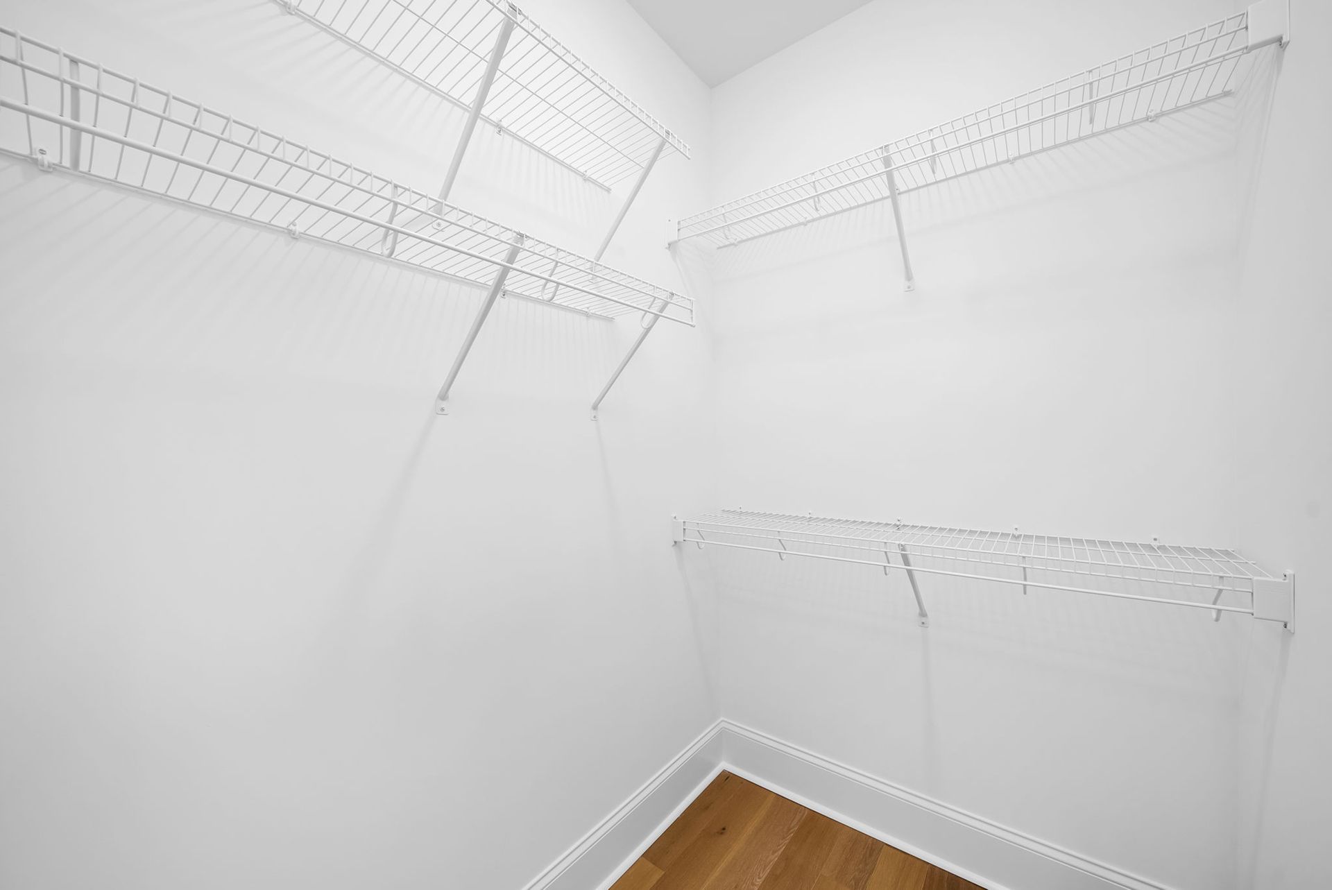 An empty walk in closet with wooden floors and white wire shelves.
