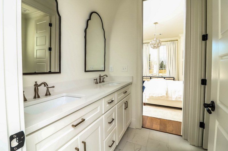 A bathroom with two sinks , a mirror and a door leading to a bedroom.