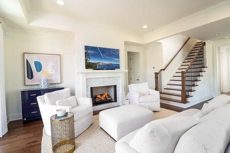 A living room with a couch , chairs , ottoman , fireplace and stairs.