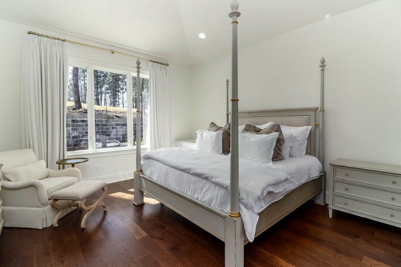 A bedroom with a four poster bed , dresser , chair and window.