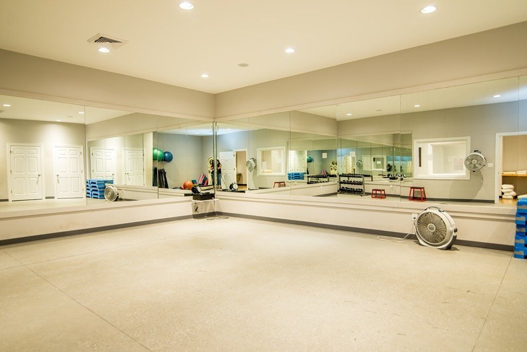 A large empty gym with lots of mirrors and a fan.