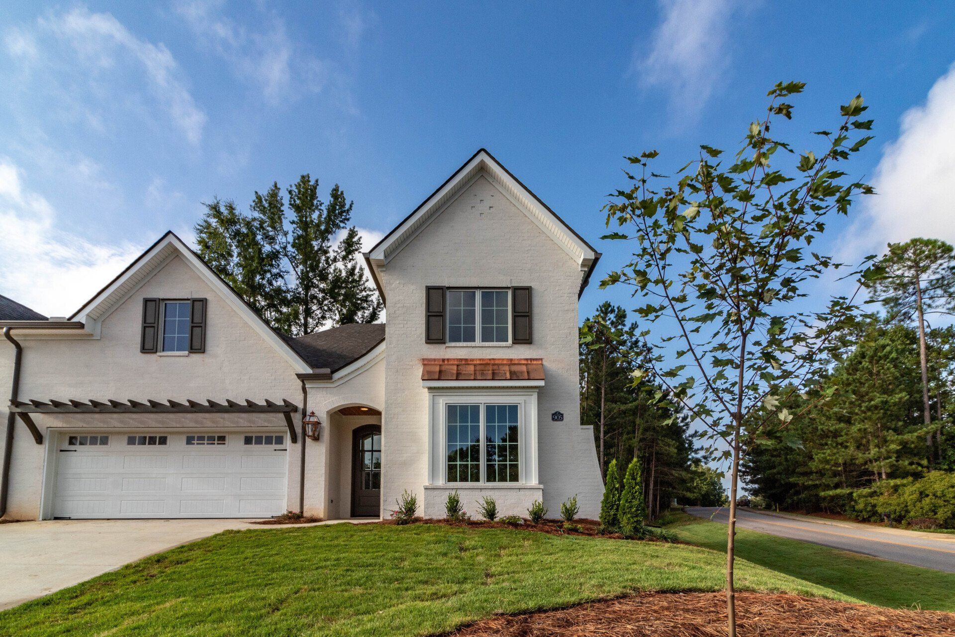 A large white house with a garage and a tree in front of it.