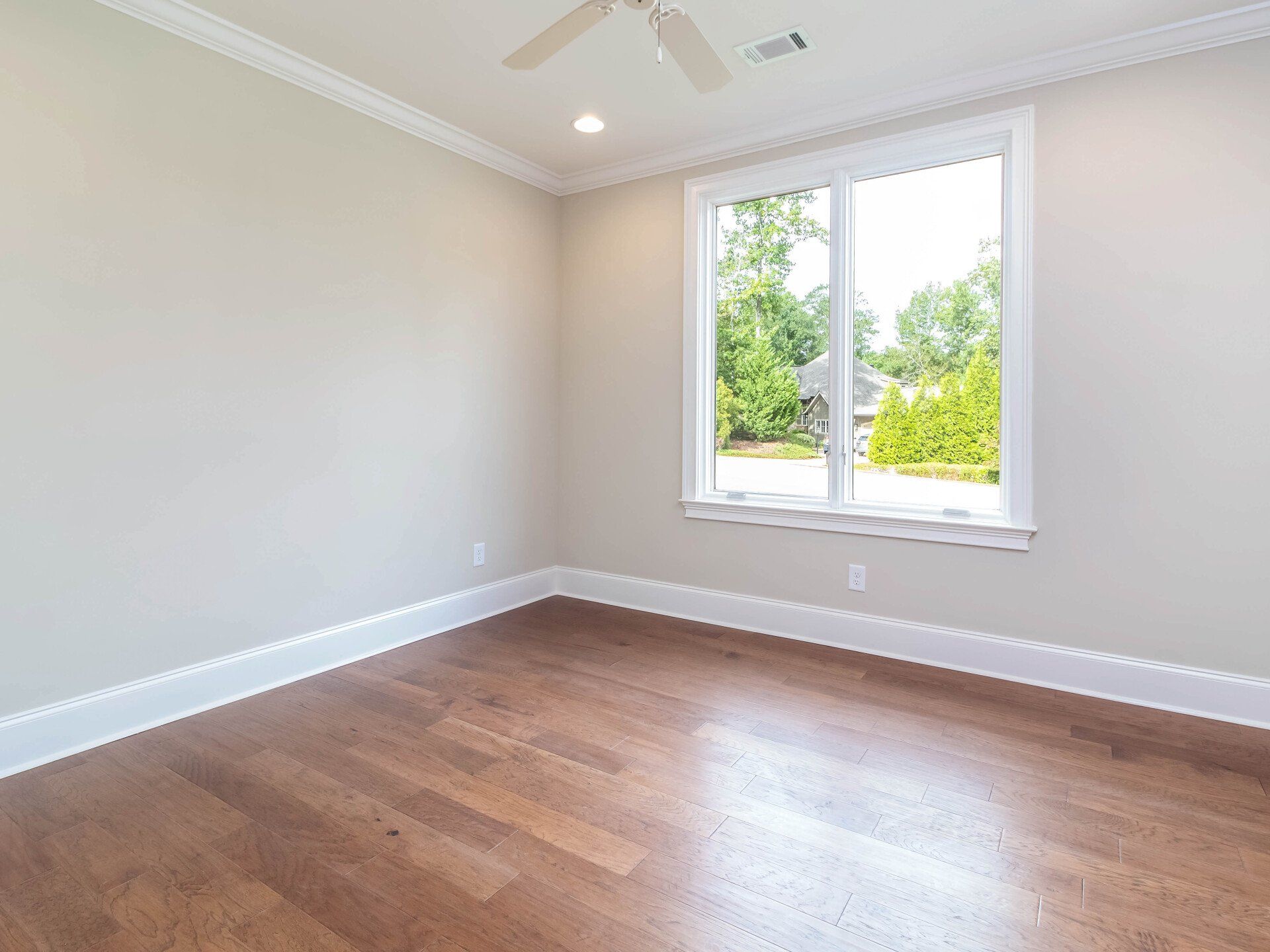 An empty bedroom with hardwood floors and a large window.