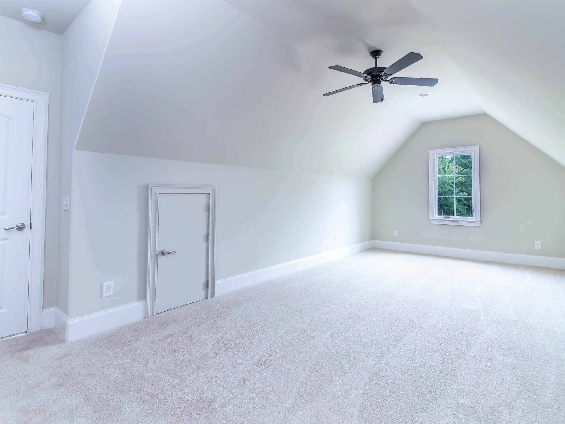 An empty room with a ceiling fan and a window.