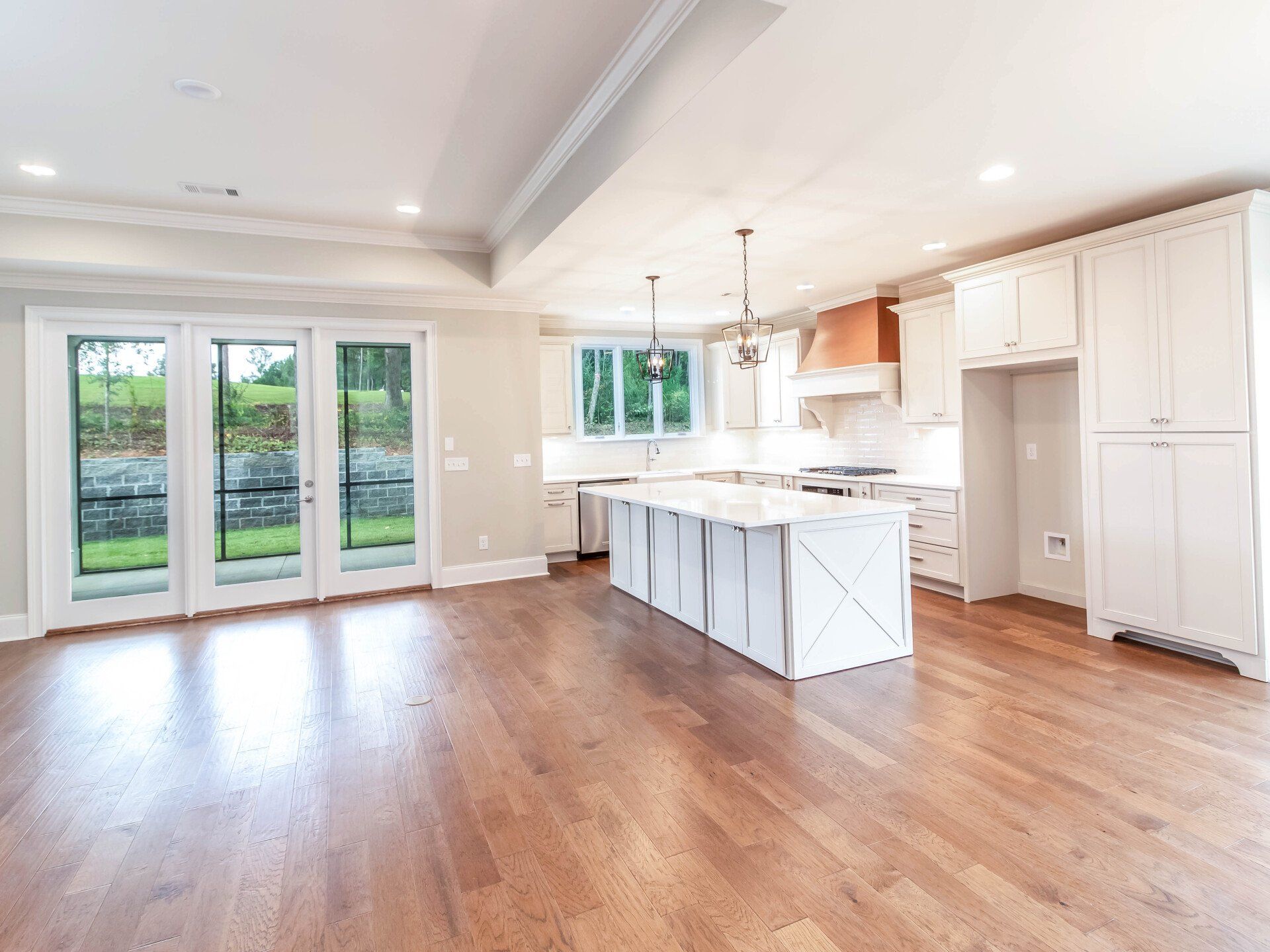 An empty kitchen with hardwood floors and white cabinets.