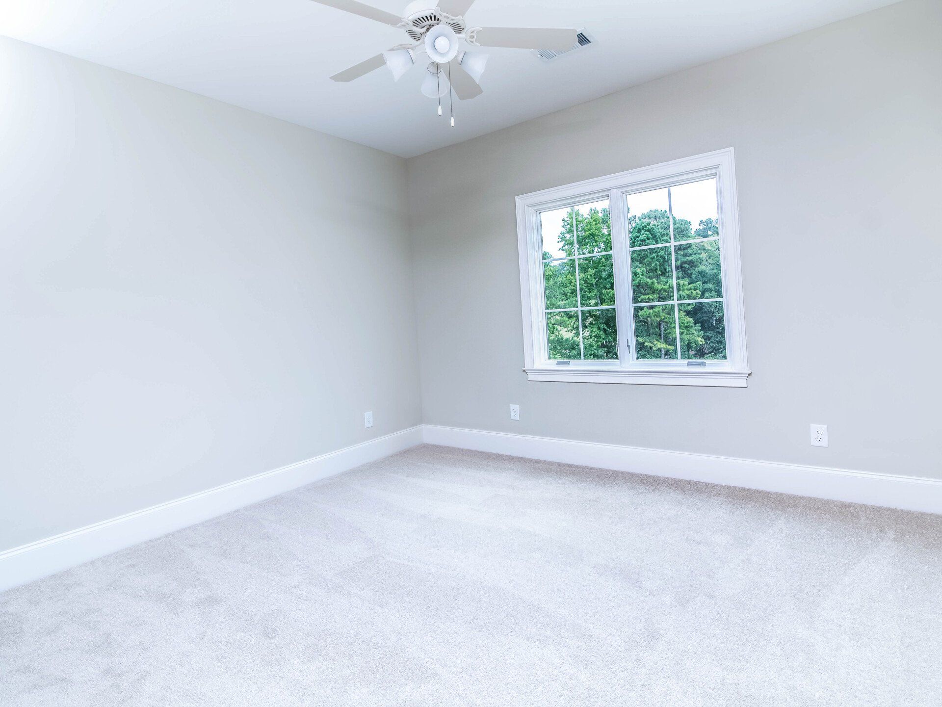 An empty bedroom with a ceiling fan and a window.