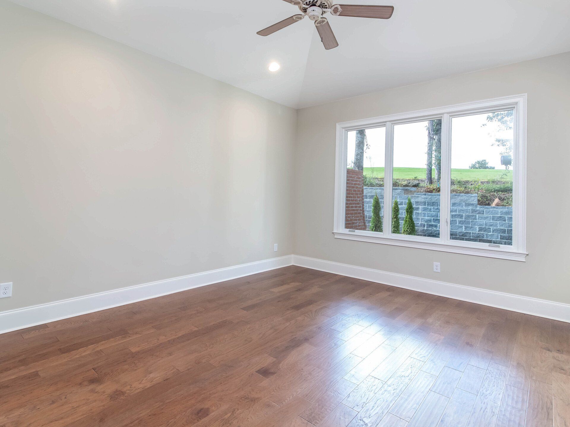 An empty room with hardwood floors and a ceiling fan.