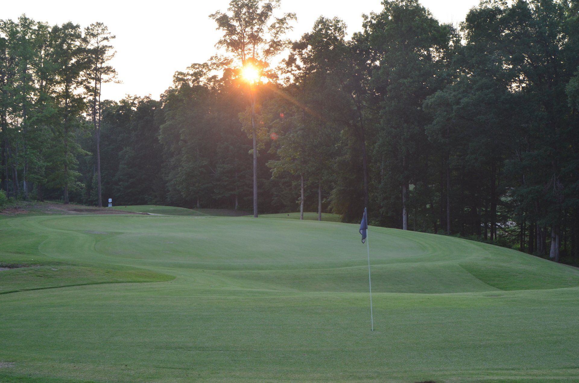The sun is setting over a golf course with trees in the background