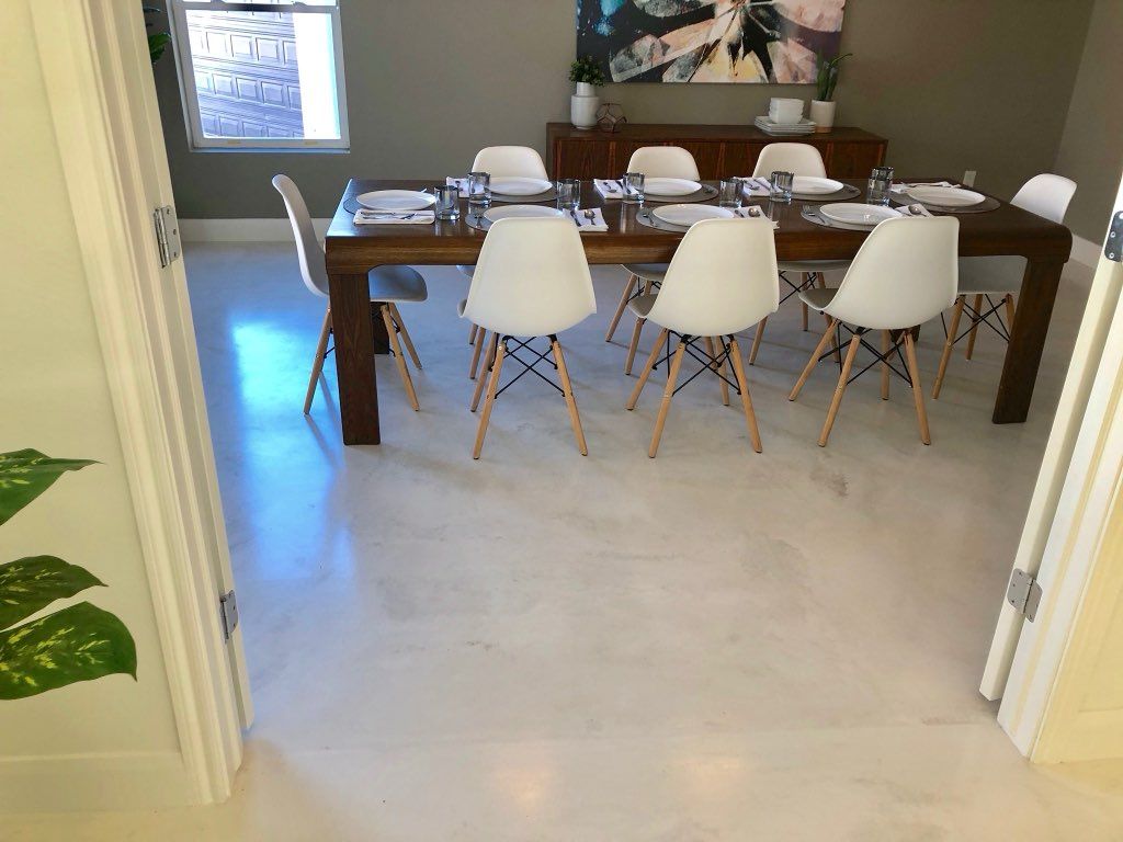 A dining room with a table and chairs and a painting on the wall.