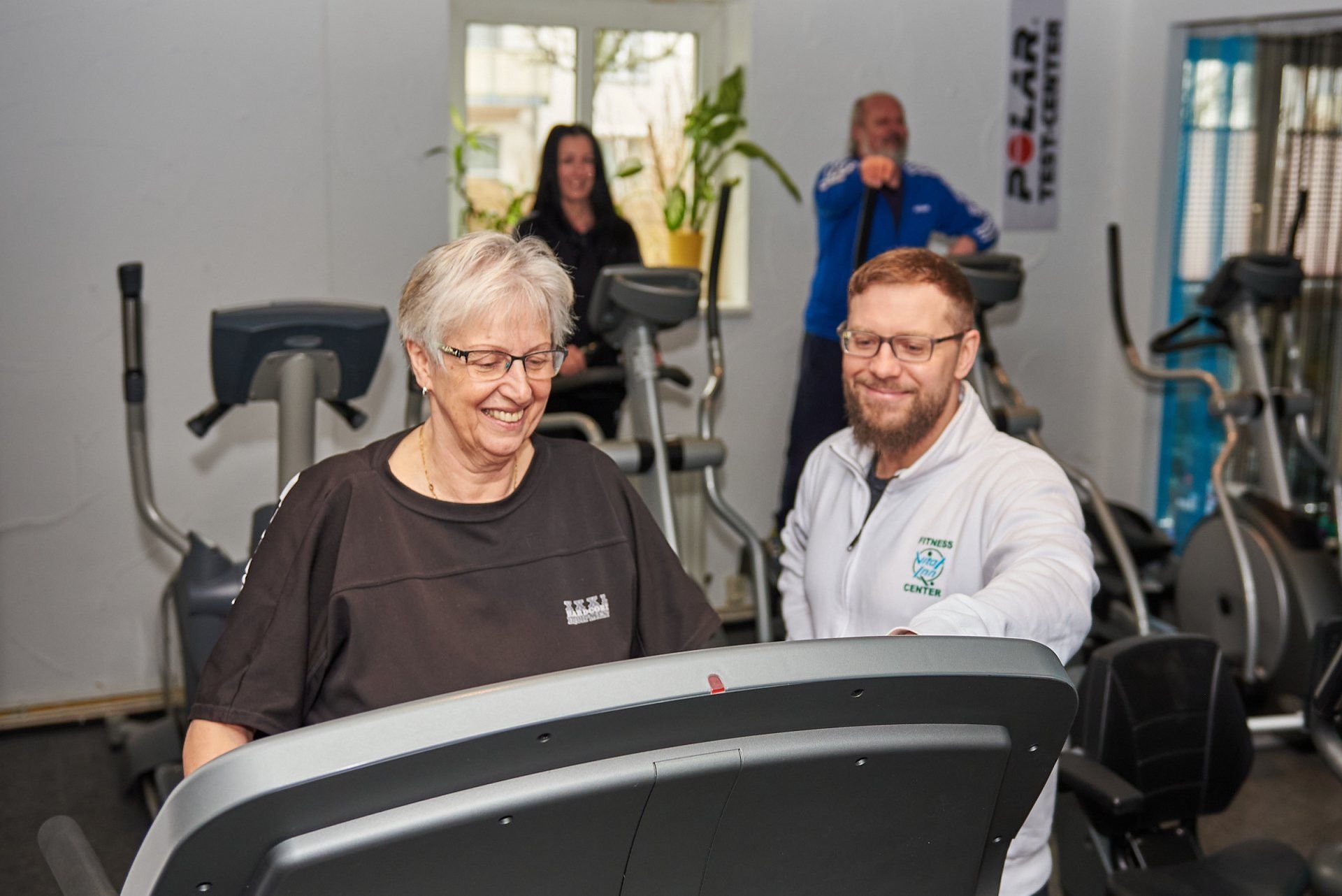 Ein Mann hilft einer Frau auf einem Laufband in einem Fitnessstudio.