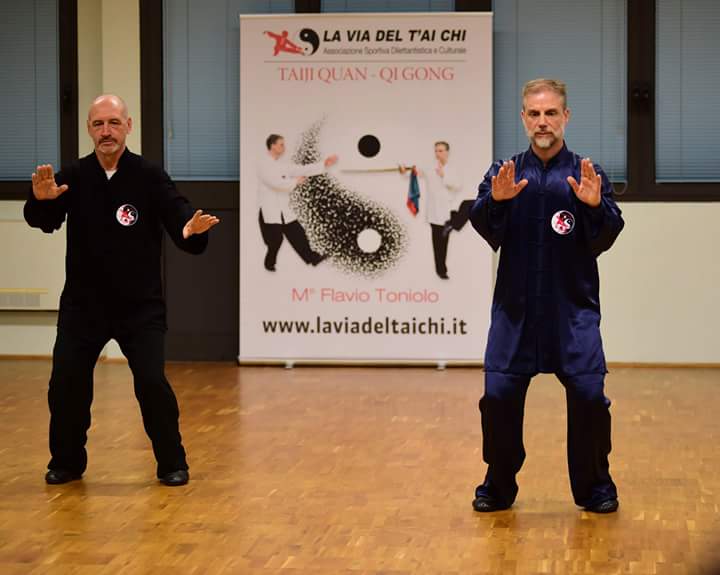 Due uomini praticano arti marziali davanti ad un cartello che dice la via del tai chi