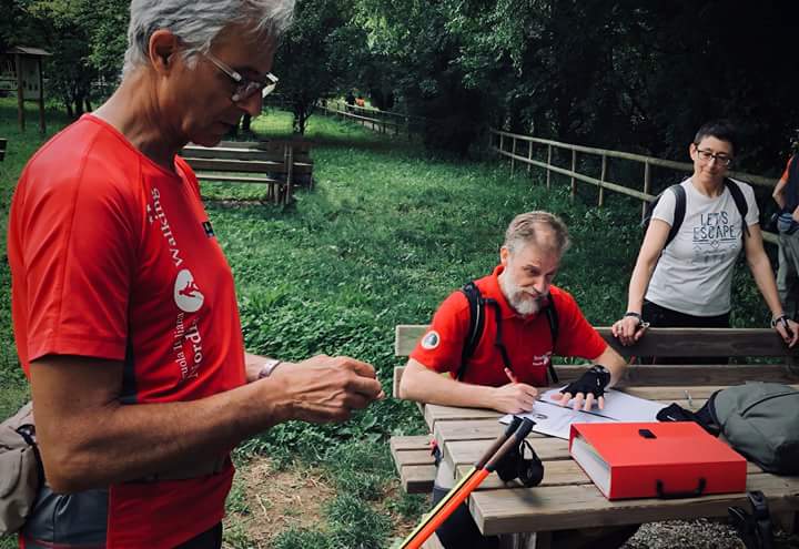 Un uomo con una camicia rossa è in piedi accanto a un uomo seduto a un tavolo da picnic.