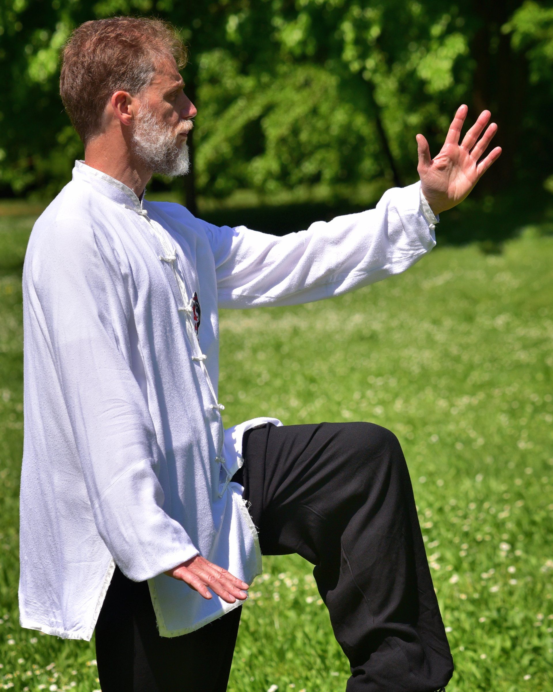 Un uomo con una camicia bianca e pantaloni neri è in piedi su una gamba sola in un campo.