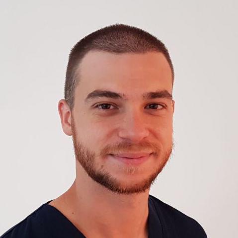 Un uomo con la barba e i capelli corti sorride alla telecamera.