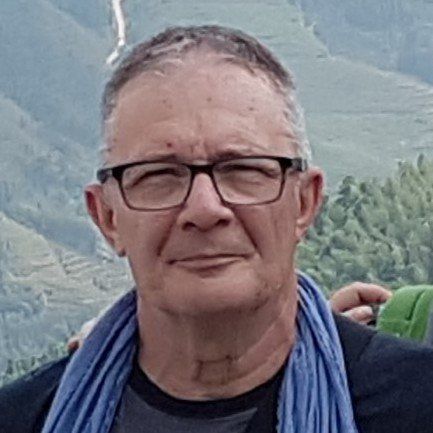 Un uomo con gli occhiali e una sciarpa blu è in piedi di fronte a una montagna.