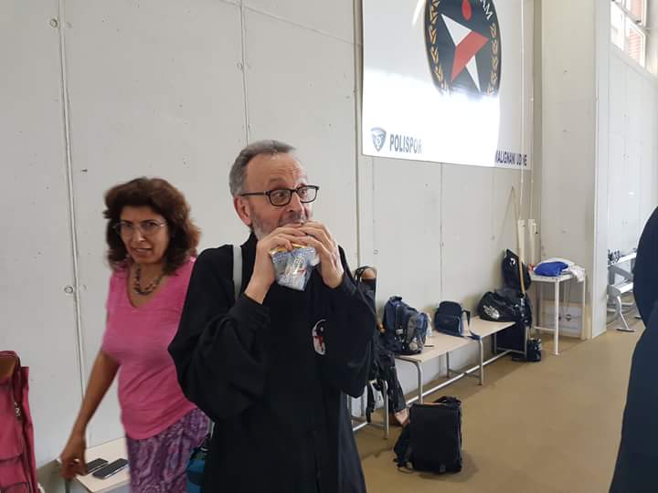 Un uomo beve acqua mentre è in piedi accanto a una donna con una maglietta rosa.