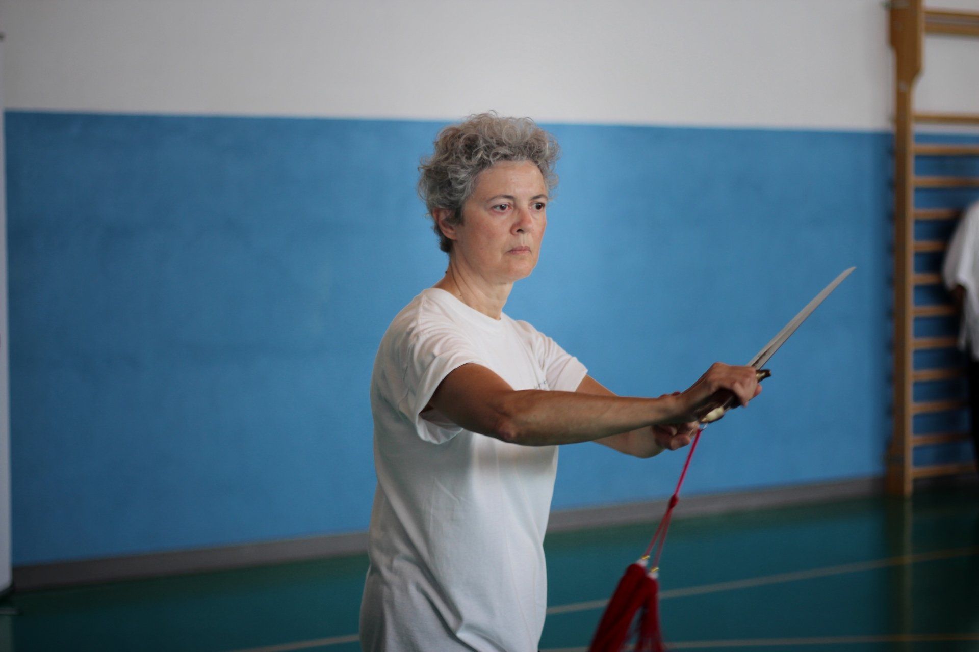 Una donna in camicia bianca tiene in mano un bastone in palestra.