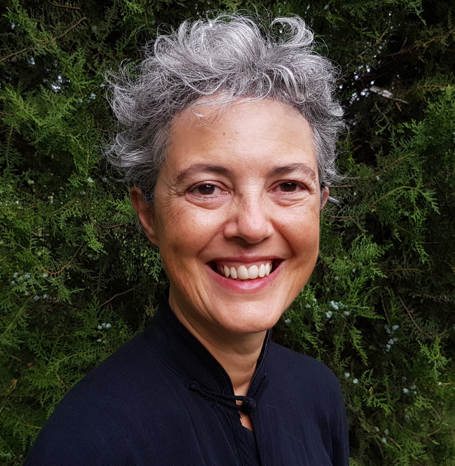 Una donna con i capelli grigi sorride davanti a un albero.