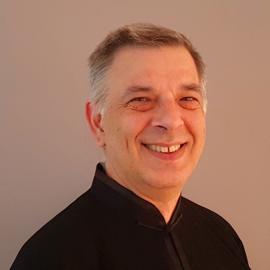 Un uomo con una camicia nera sorride alla telecamera.