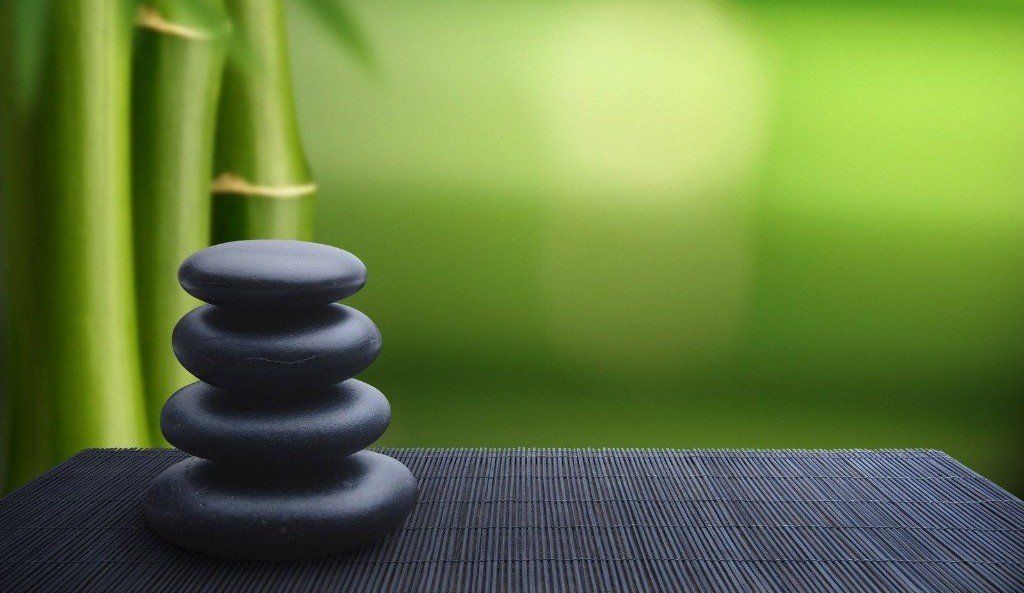 Una pila di rocce nere seduta sopra un tavolo di legno con bambù sullo sfondo.