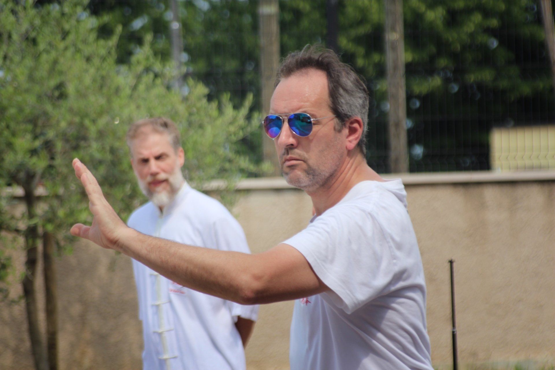 Un uomo che indossa occhiali da sole e una camicia bianca è in piedi davanti a un muro.