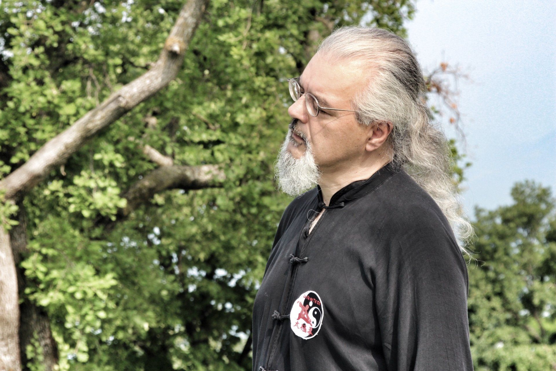 Un uomo con i capelli lunghi e la barba è in piedi davanti a un albero.