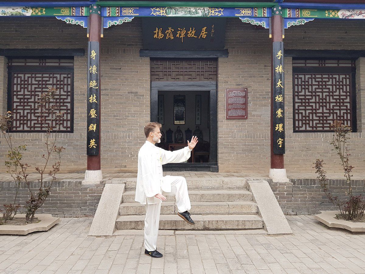 Un uomo pratica arti marziali davanti a un edificio con scritte cinesi sopra