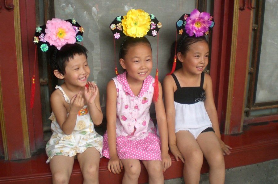 Tre bambine sono sedute una accanto all'altra con dei fiori tra i capelli.