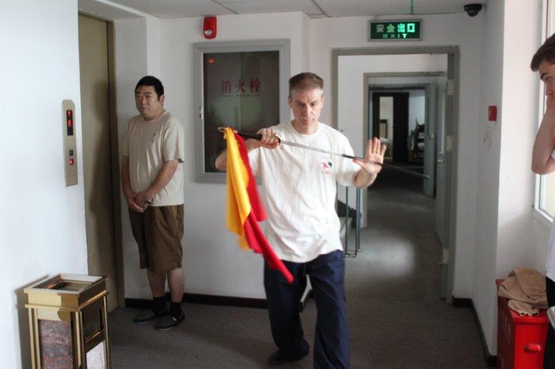 Un uomo in camicia bianca tiene in mano una bandiera rossa e gialla in un corridoio.