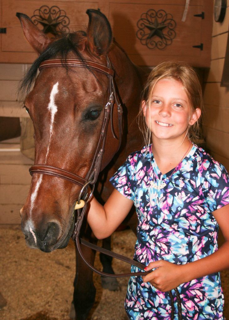 A young girl is standing next to a brown horse