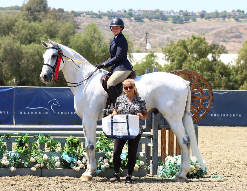 A woman is standing next to a white horse.