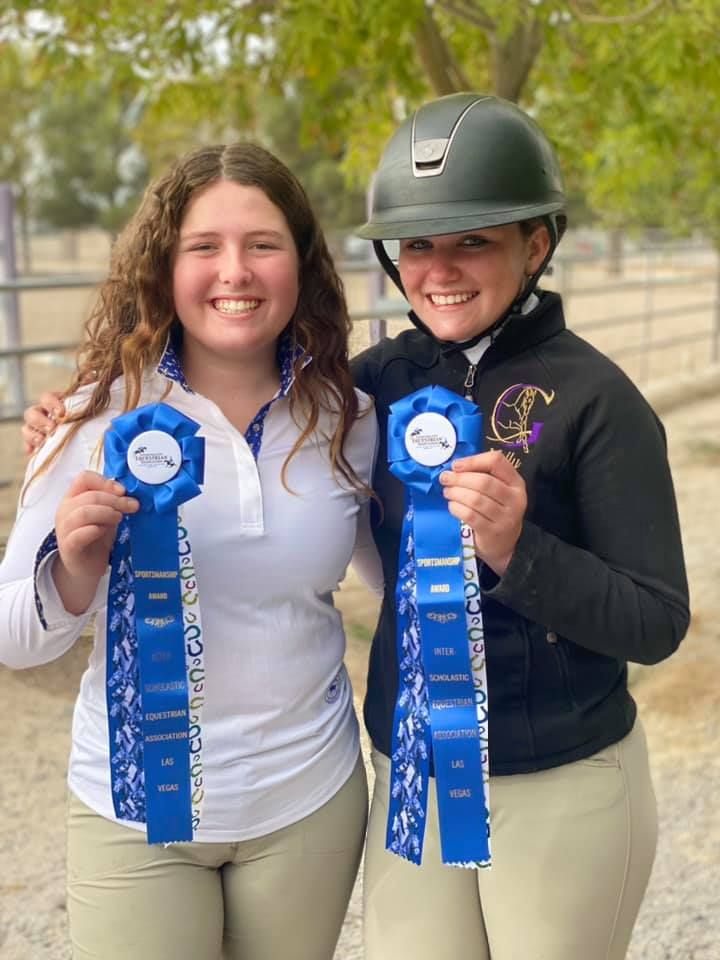 Two young women are standing next to each other holding blue ribbons.