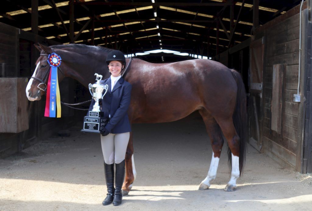 A woman is standing next to a horse holding a trophy.