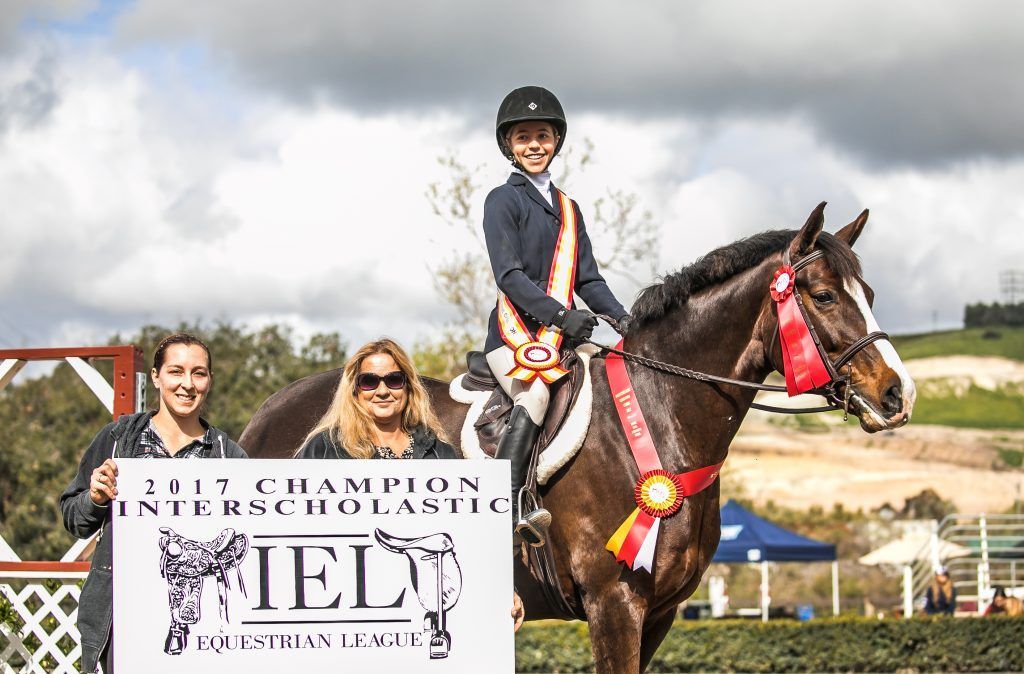 A person is riding a horse in front of a sign that says ' ielt ' on it.