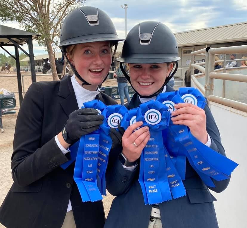 Two women wearing helmets are holding blue ribbons