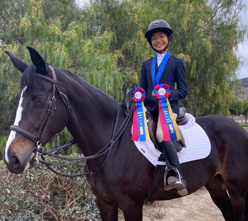 A young girl is riding a horse with ribbons around her neck