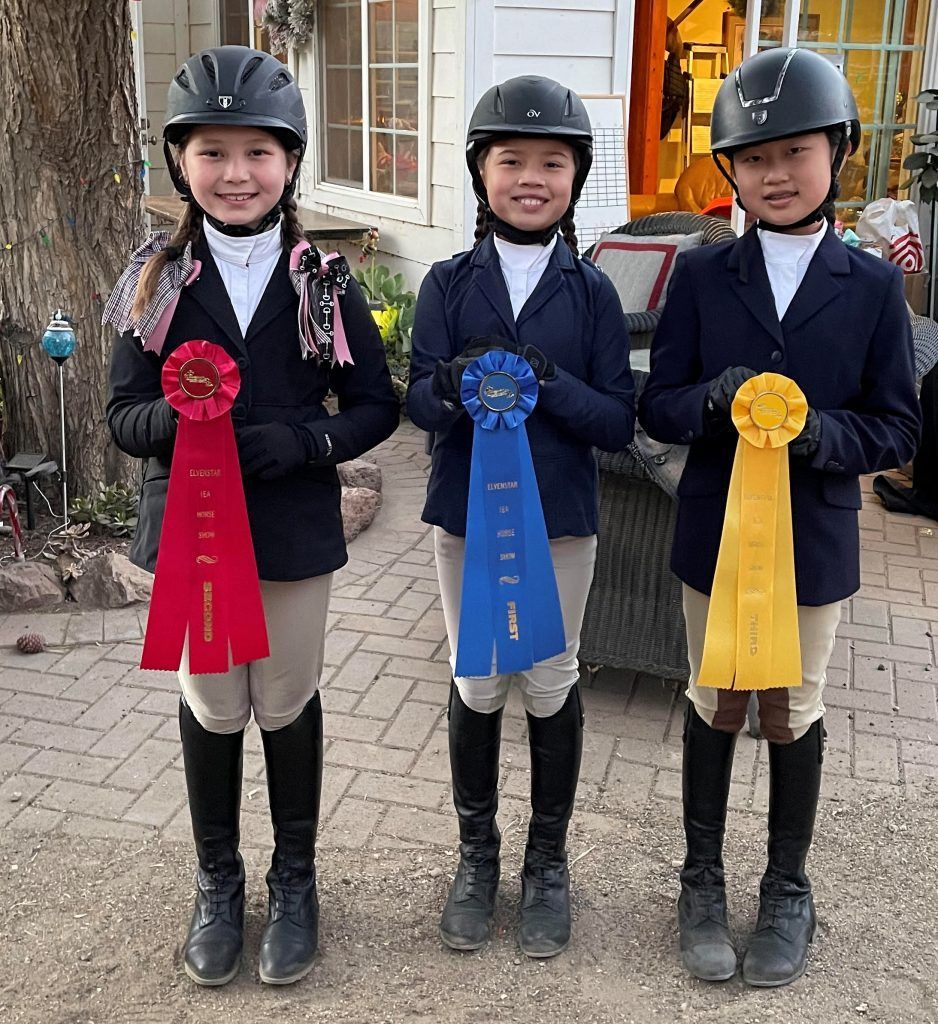 Three young girls are standing next to each other holding ribbons