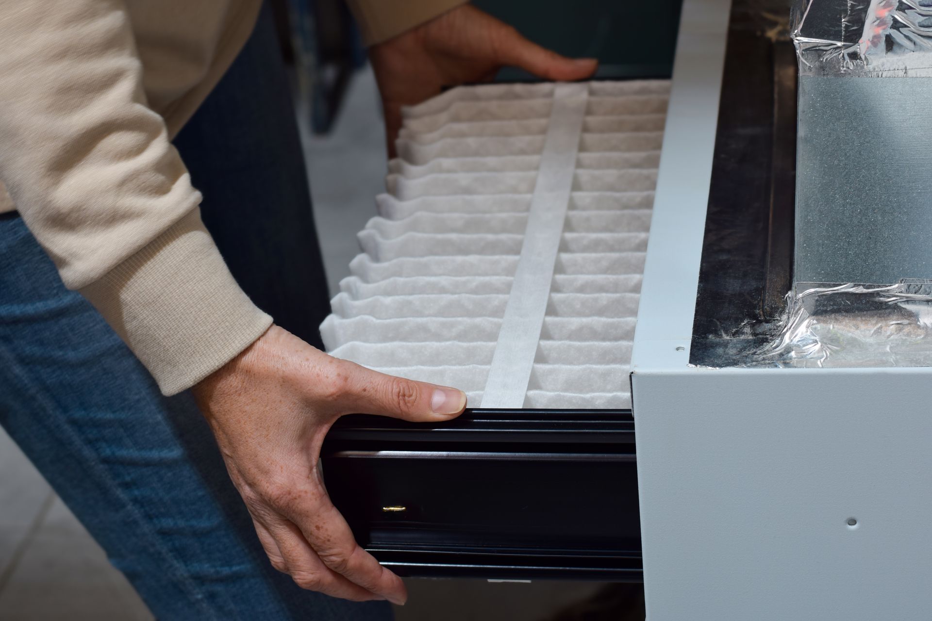 Person replacing a white air filter in a furnace.