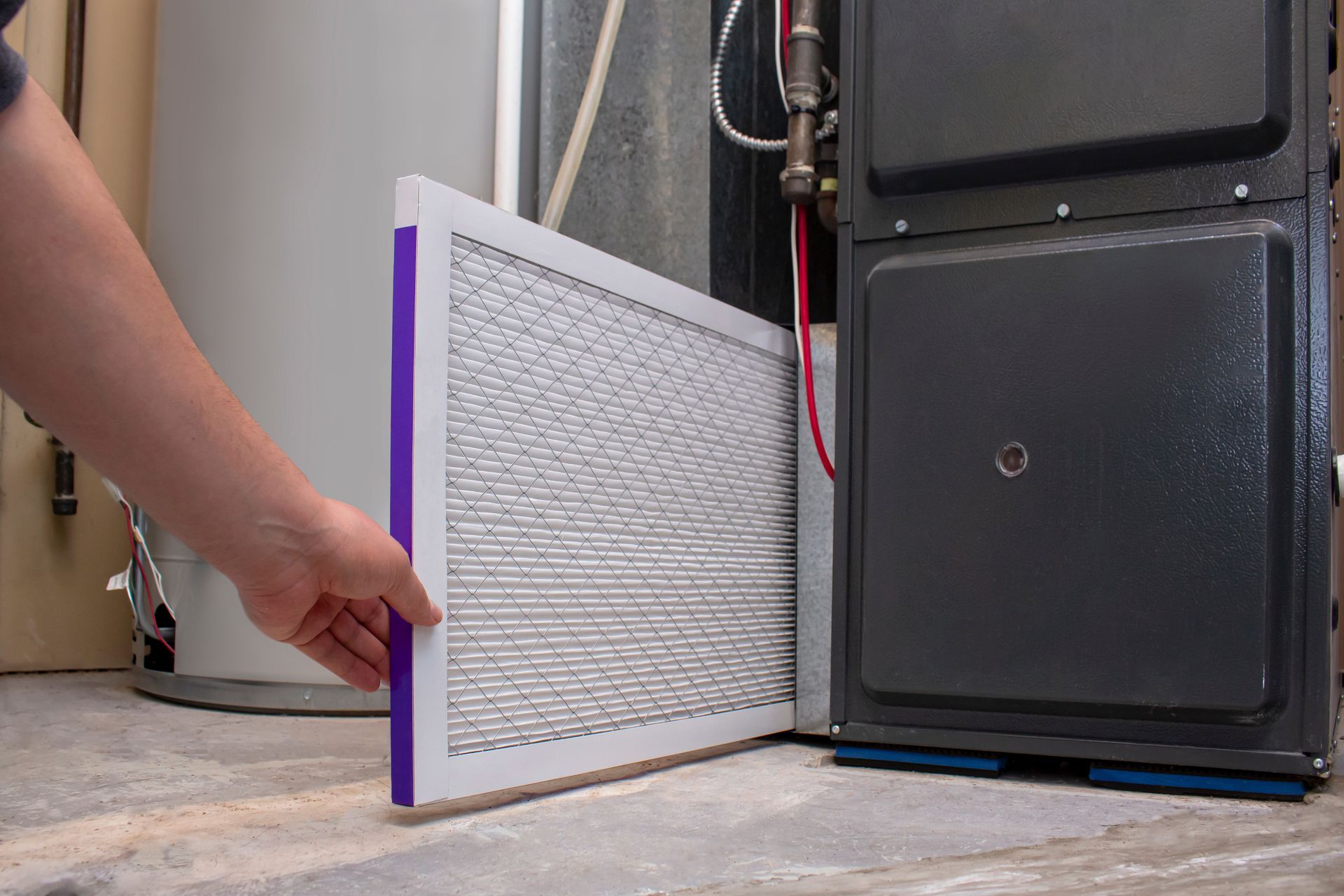 Hand removing a rectangular furnace filter from a dark gray furnace.