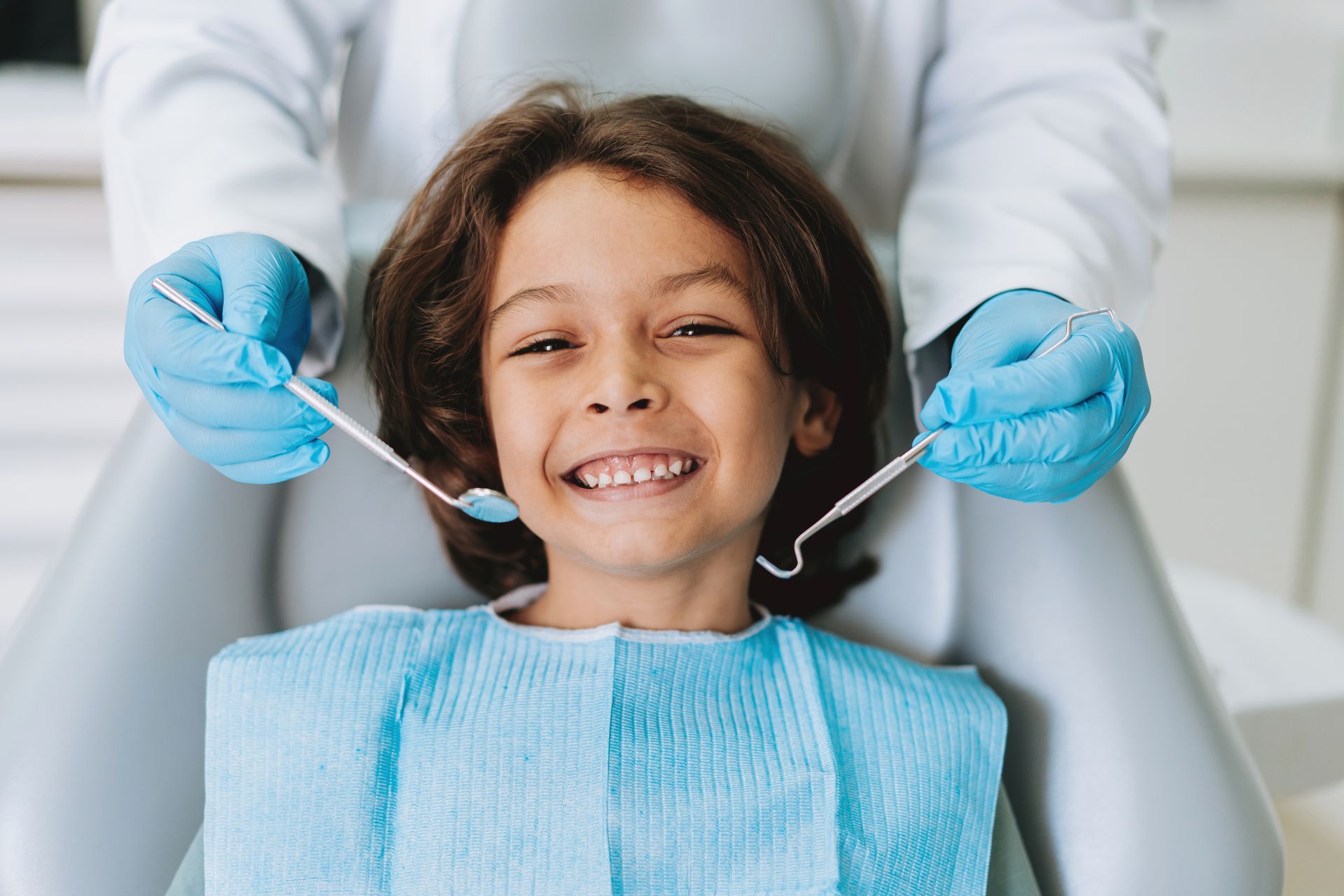 Smiling child sitting in dental chair during routine kids dentistry checkup with dentist.