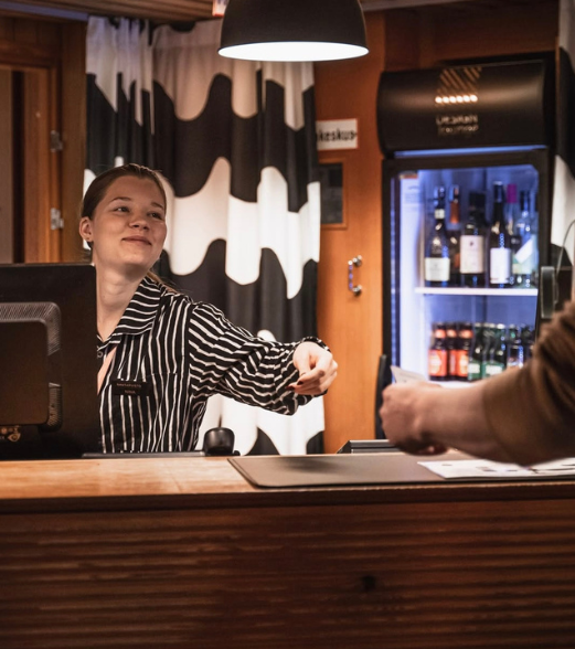 A staff member in a striped shirt reaching across a reception counter to accept a card from a customer.