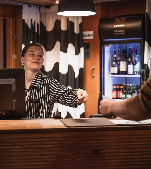 Raidalliseen paitaan pukeutunut henkilö ojentaa kätensä tiskin yli ottaakseen kortin asiakkaalta vastaanottoalueella.