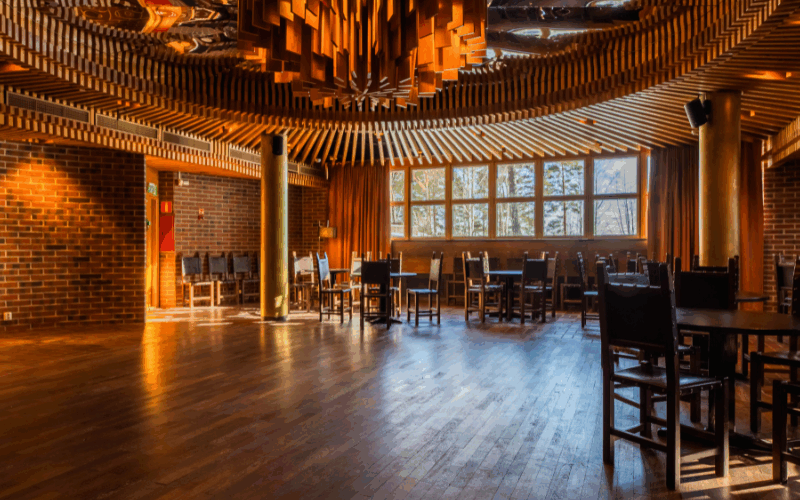 Tilava ravintolasisustus, jossa on puulattiat, tiiliseinät, pyöreä valaistus ja ruokapöydät tummine tuoleineen.