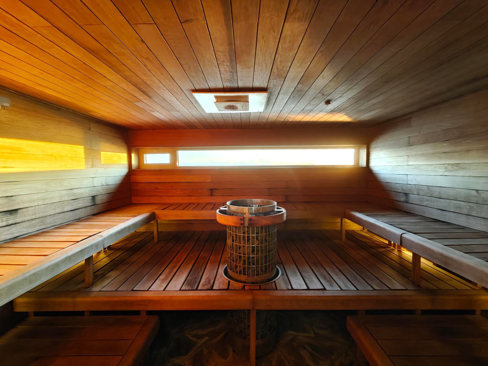Modern wooden sauna interior with a central heater and two levels of bench seating bathed in warm, soft lighting.